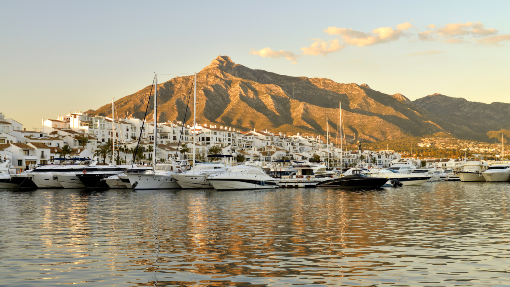 Luxury yachts in Puerto Banús Marina with Marbella's La Concha mountain rising in the background during golden hour.